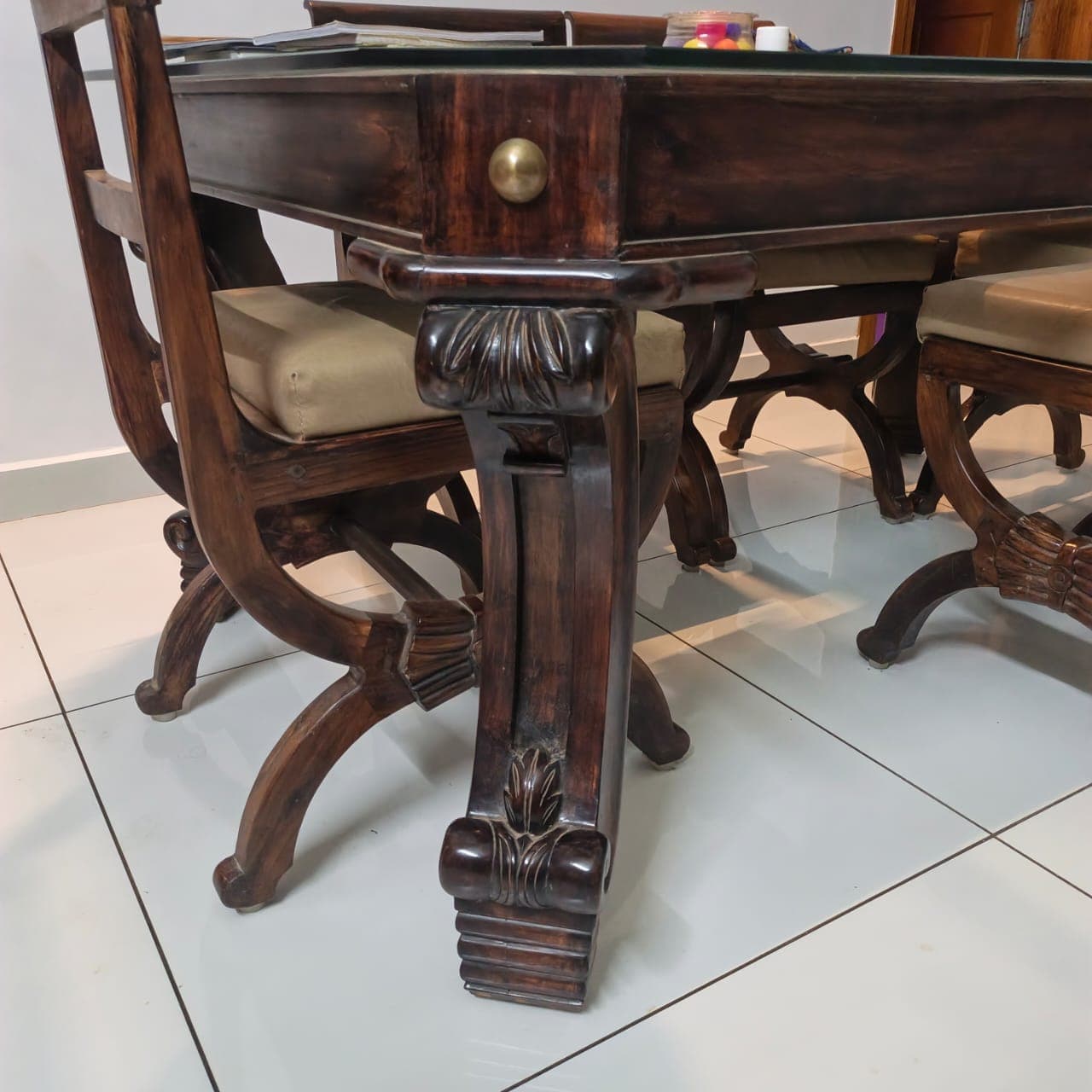 Close-up of a dark polished wooden dining table leg with hand-carved scroll and leaf detail and a brass knob