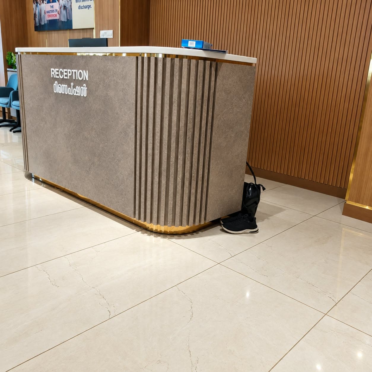 Reception desk with stone-finish fluted panels, rounded corners, brass base trim and white top, in front of a wooden slat wall