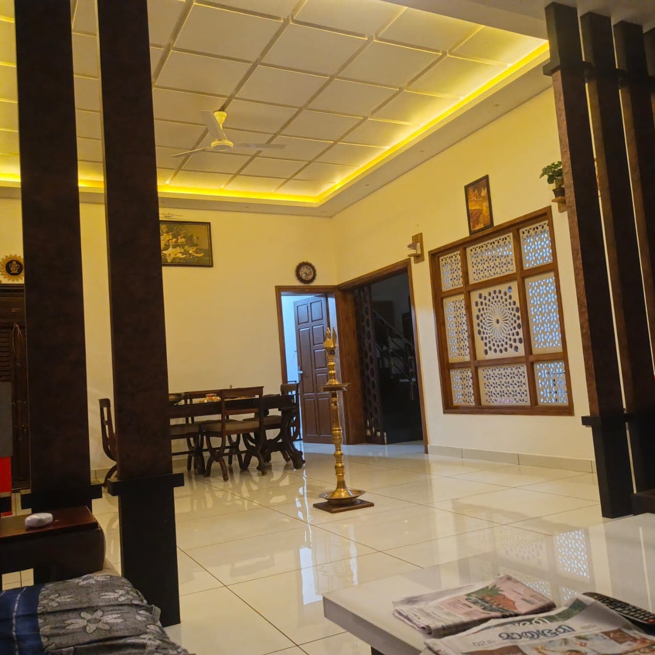 Kerala living and dining room with grid-pattern false ceiling, warm cove lighting, wooden jali window panel and pillar partition