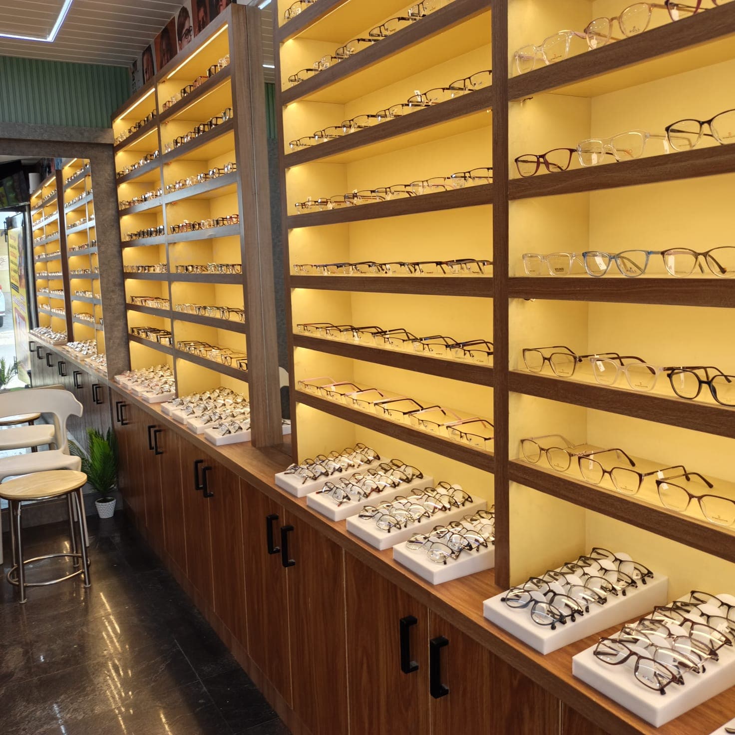 Long Lens & Lark optical store wall of warm backlit eyewear shelves with display trays on a walnut counter
