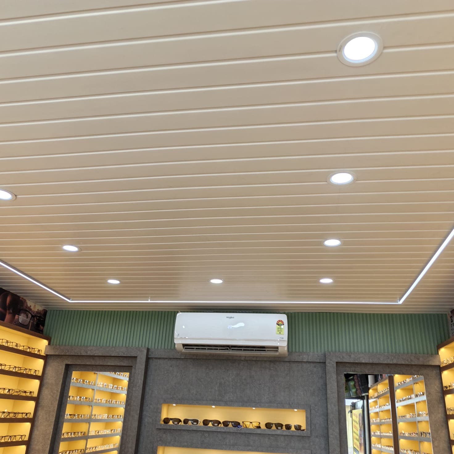 Lens & Lark optical store ceiling in grooved panels with round downlights and a continuous LED profile border, above lit display walls