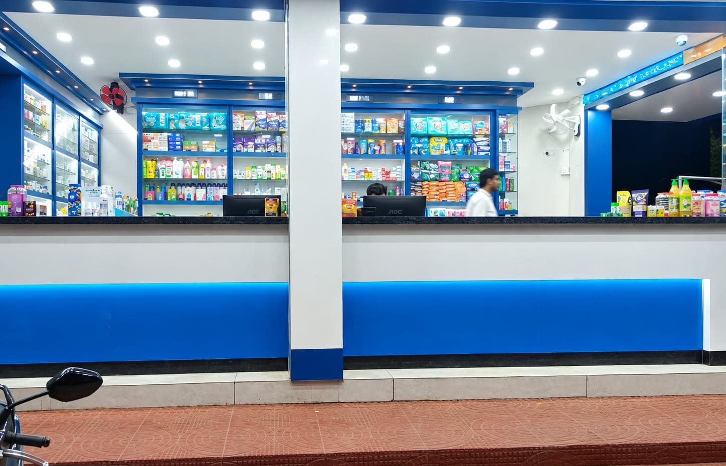 Novus Medicals pharmacy service counter with granite top and backlit blue band, and lit display shelving behind