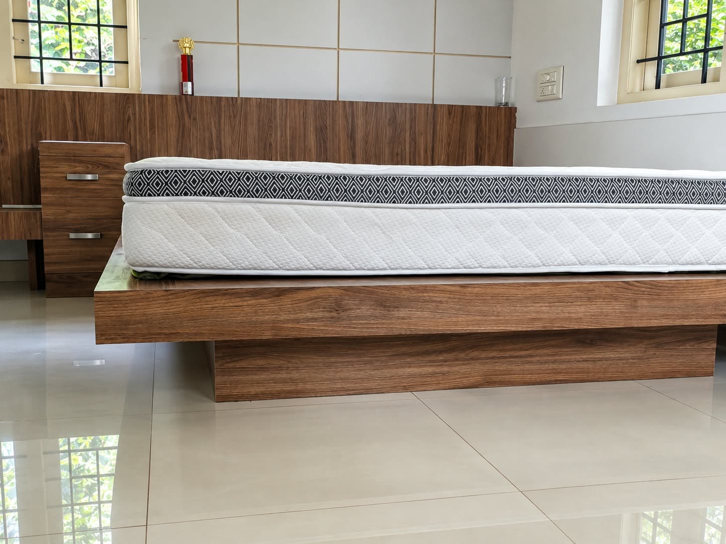 Walnut-finish platform bed on a recessed floating plinth, with matching side drawer unit and wall-length headboard panel